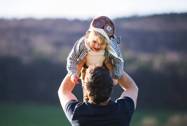 Um pai levantando seu filho criança no ar fora na natureza primavera . — Fotografia de Stock