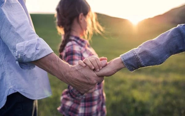 A small girl with her senior grandparents holding hands outside in nature at sunset. — Stock Photo, Image