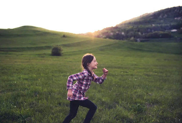 En liten flicka som kör utanför i naturen vid solnedgången. — Stockfoto