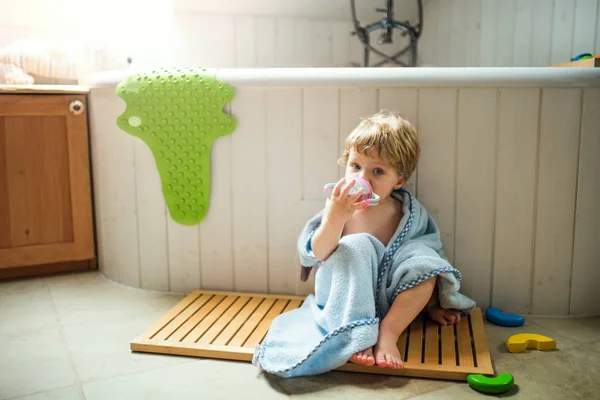 Zabalené v ručníku, sedí na podlaze v koupelně doma batole chlapec. — Stock fotografie