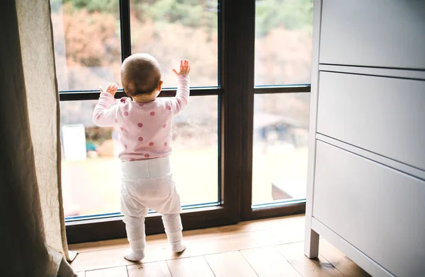 Ett småbarn barn står vid fönstret på golvet hemma. — Stockfoto