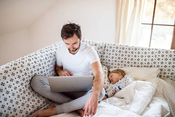 Padre con portátil y un niño durmiendo en la cama en casa . — Foto de Stock