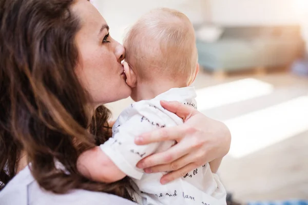 Porträtt av en ung mamma kysser hennes baby-son hemma. Närbild. — Stockfoto