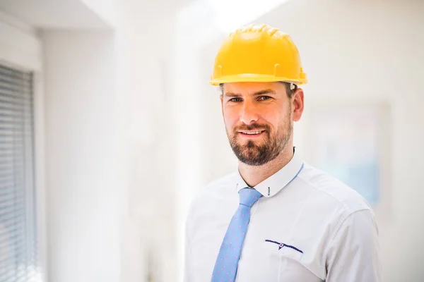 Um jovem engenheiro ou arquiteto com camisa branca, gravata e capacete em uma sala . — Fotografia de Stock