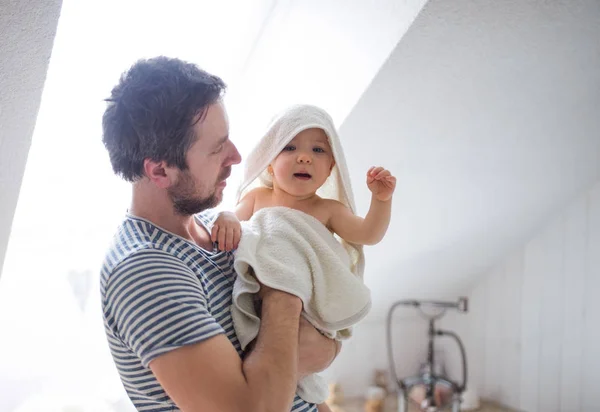 Padre con un niño pequeño envuelto en toalla en un baño en casa . —  Fotos de Stock