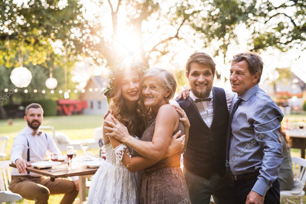 Bride, groom with parents posing for the photo at wedding reception outside in the backyard.