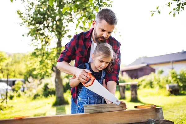 Padre e una piccola figlia con una sega all'esterno, facendo birdhouse in legno . — Foto Stock