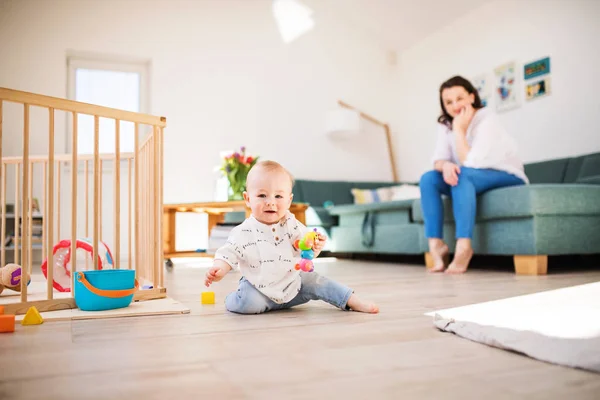 Een babyjongen spelen op de vloer thuis, moeder op de achtergrond. — Stockfoto