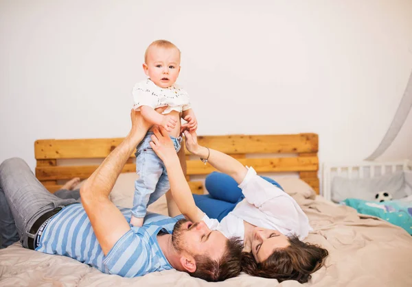 若い家族は、自宅で男の子の赤ちゃんとベッドで横になっています。. — ストック写真