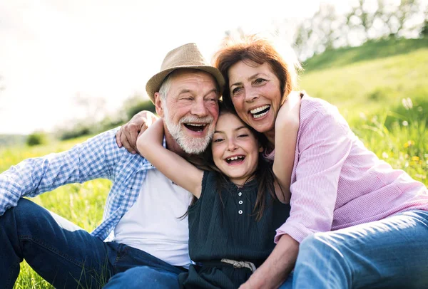 Seniorenpaar mit Enkelin im Frühling draußen in der Natur, im Gras entspannen. — Stockfoto