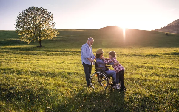 A small girl with her senior grandparents with wheelchair on a walk outside in nature. — Stock Photo, Image