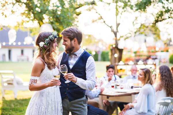 Bride and groom clinking glasses at wedding reception outside in the backyard.