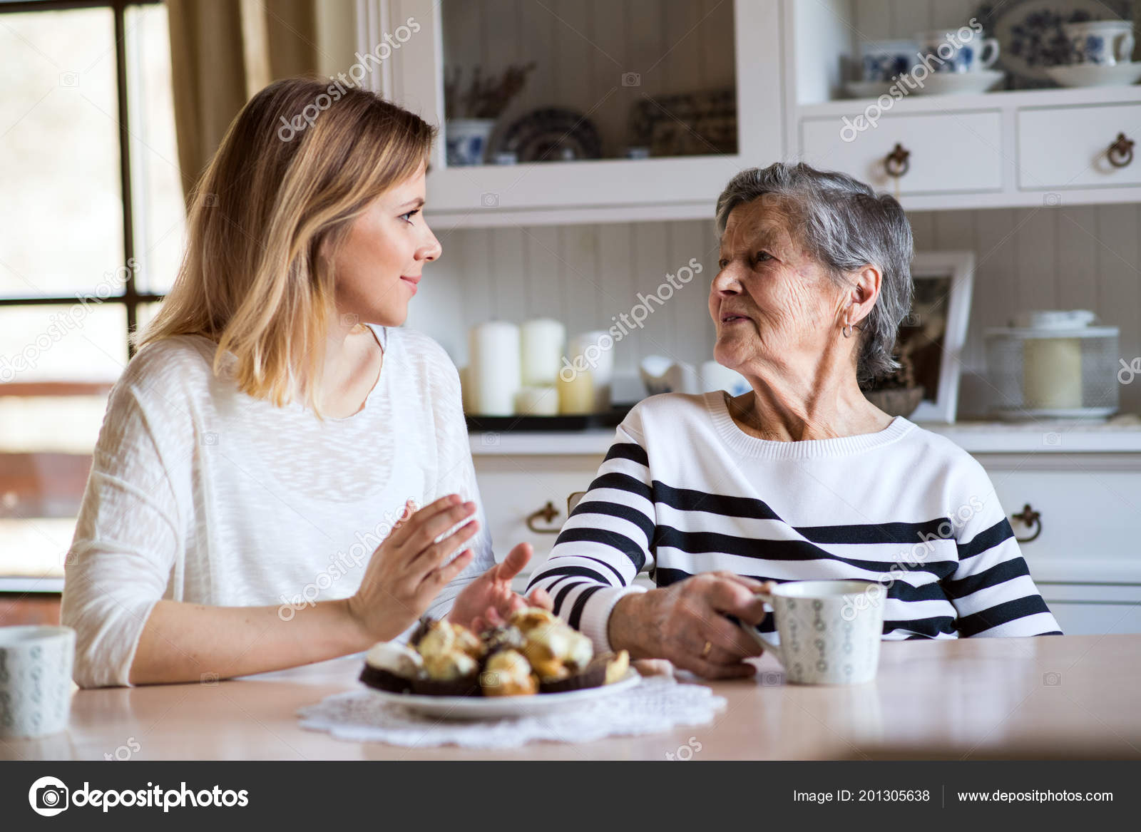 An elderly grandmother with an adult granddaughter sitting at the table ...