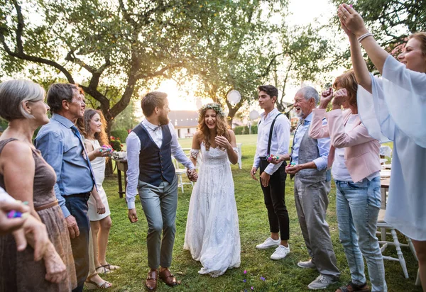 Bruden, brudgummen och gäster på bröllop mottagning utanför i trädgården. — Stockfoto