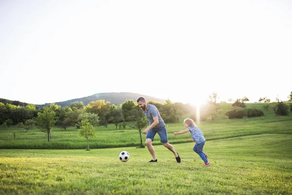 Padre con una pequeña hija jugando con una pelota en la naturaleza de primavera . — Foto de Stock
