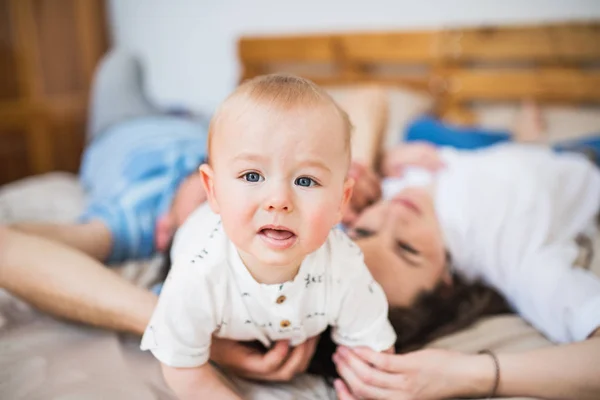 Baby boy w domu na łóżku z rodzicami nie do poznania. — Zdjęcie stockowe