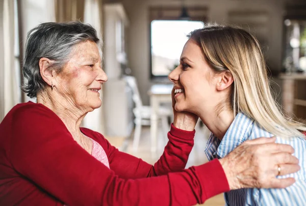 Een bejaarde oma te kijken naar een volwassen kleindochter thuis. — Stockfoto