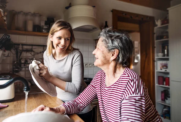 Una abuela anciana con una nieta adulta en casa, lavando los platos . — Foto de Stock