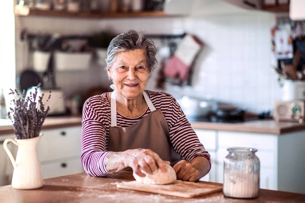 Une femme âgée pétrissant de la pâte dans la cuisine à la maison . — Photo