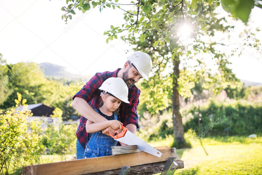 Father and a small daughter with a saw outside, cutting wood.