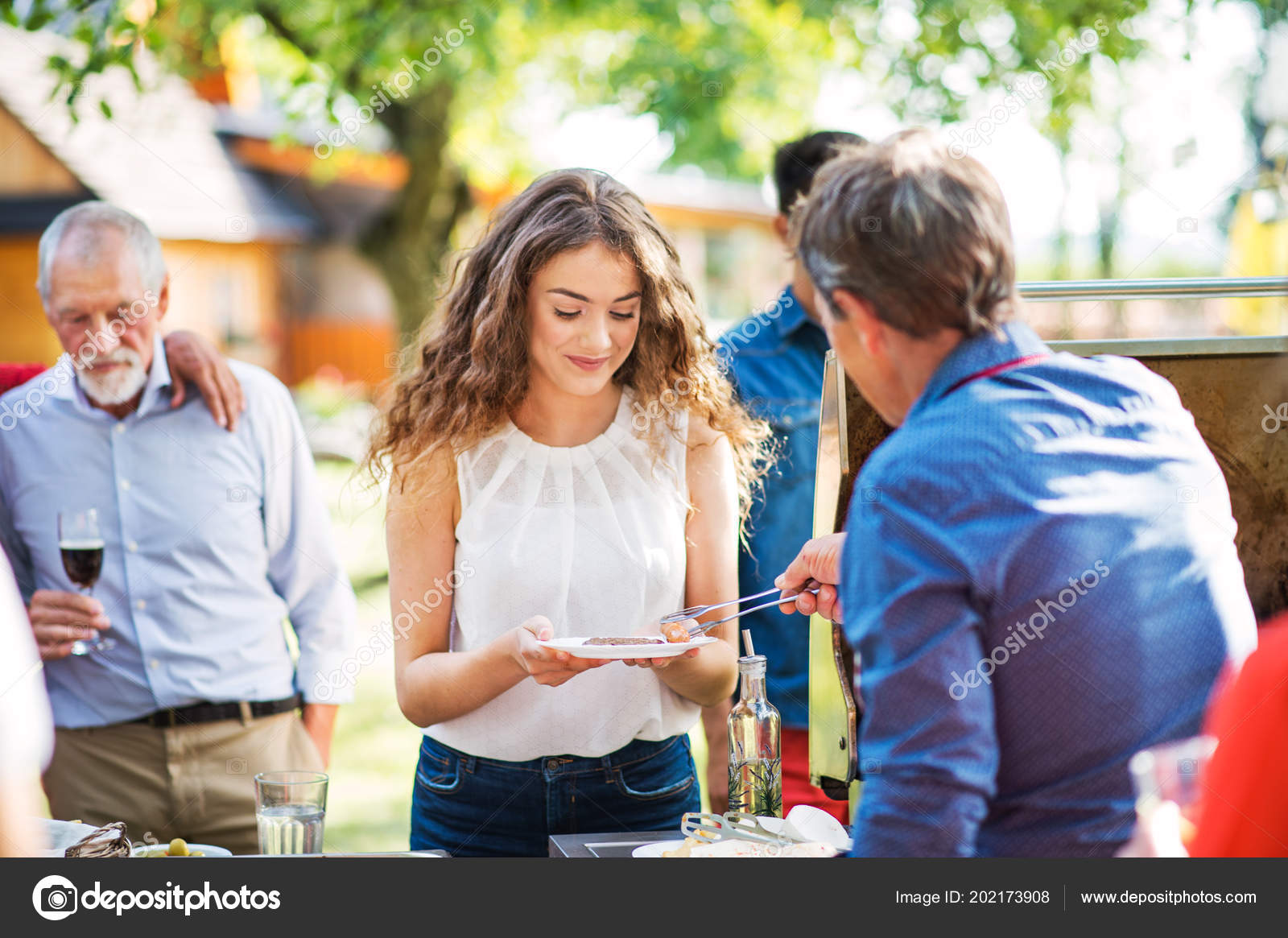 A senior man cooking and serving food on a barbecue party outside in the backyard. Stock Photo