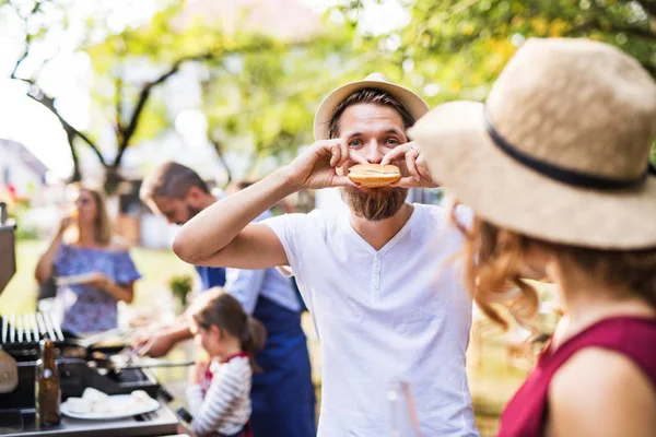 Un joven comiendo una hamburguesa en una celebración familiar o una fiesta de barbacoa afuera . —  Fotos de Stock