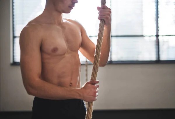 Fit young man in gym standing topless , holding climbing rope. — Stock Photo, Image