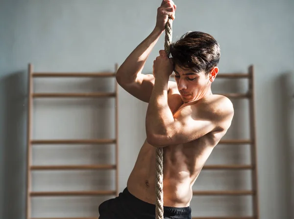 Fit young topless man in gym climbing a rope. — Stock Photo, Image