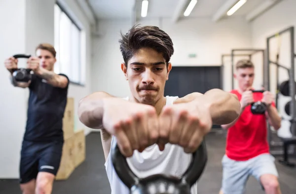 Tre unga män i gymmet gör kettlebell gungor. — Stockfoto