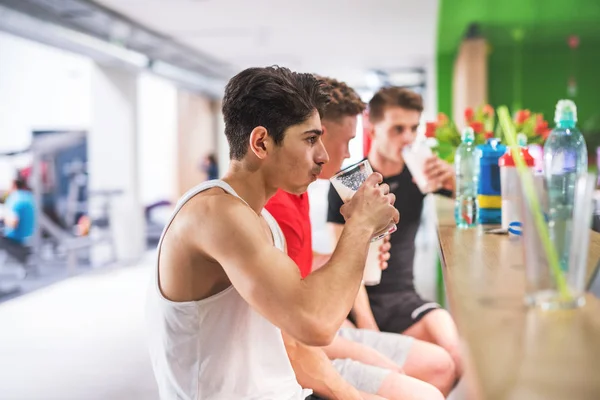 앉아서 단백질 음료 잔을 들고 체육관에서 남자. — 스톡 사진
