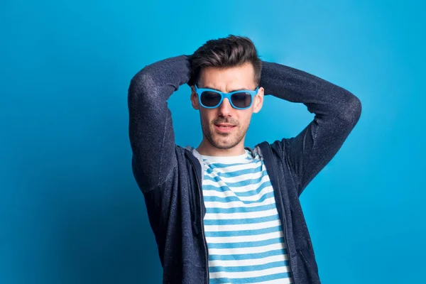 Portrait of a young man in a studio with sunglasses on a blue background. — Stock Photo, Image