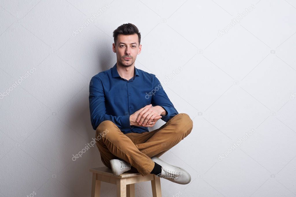 Portrait of a young man in a studio sitting on a stool.