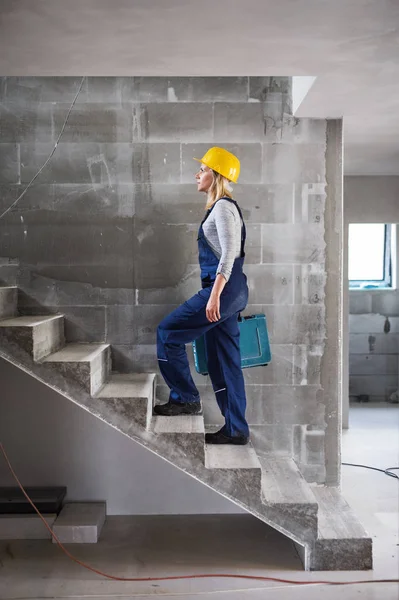Mulher trabalhadora com uma caixa de ferramentas subindo as escadas no canteiro de obras . — Fotografia de Stock