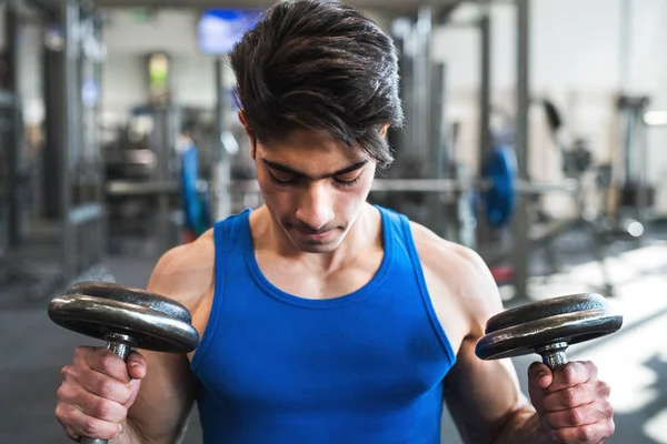 Joven hombre hispano en forma en el gimnasio haciendo ejercicio con pesas . — Foto de Stock