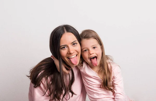 En liten flicka och hennes mamma sticker tungor ut i en studio. — Stockfoto