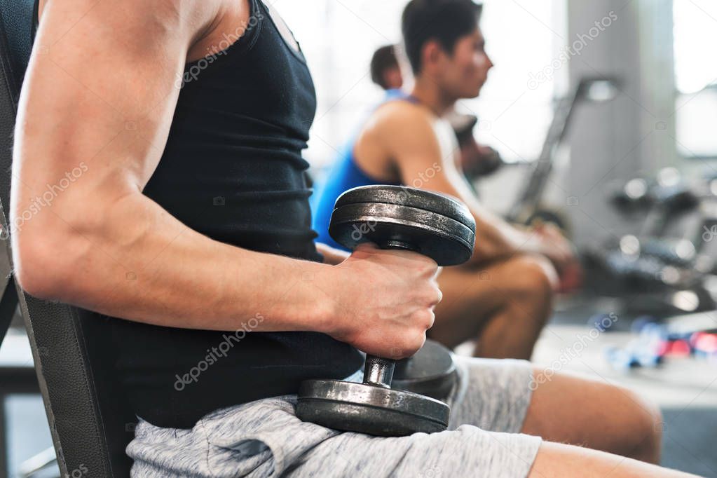 Unrecognizable young fit men in gym exercising with dumbbells.