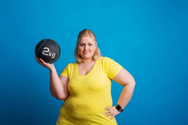 スタジオで重いボールを保持している幸せ太りすぎ女性の肖像画. — ストック写真