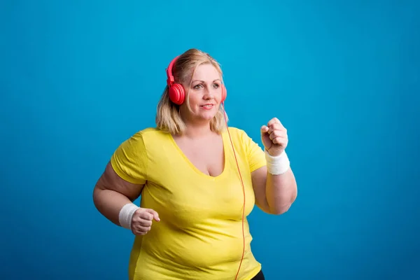 Retrato de una atractiva mujer con sobrepeso en el estudio sobre un fondo azul, trotando . —  Fotos de Stock