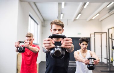 Kettlebell salıncaklar yapıyor spor salonunda üç genç adam.