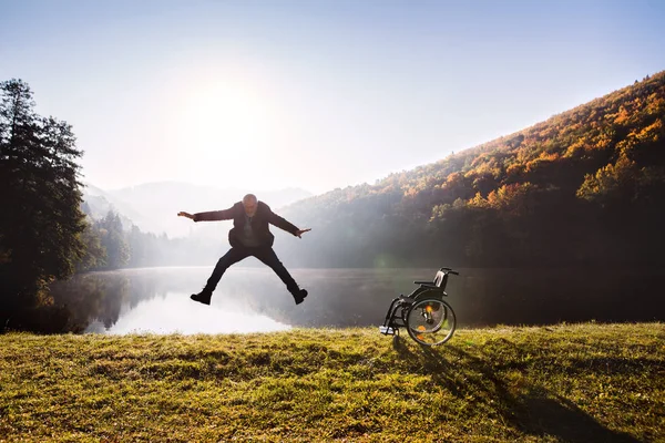 Senior man jumping by the wheelchair in autumn nature. — Stock Photo, Image