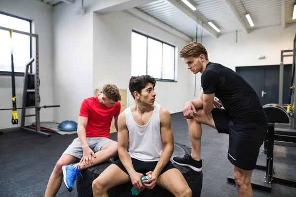 Junge Männer im Fitnessstudio reden und ruhen sich nach einer Übung aus. — Stockfoto