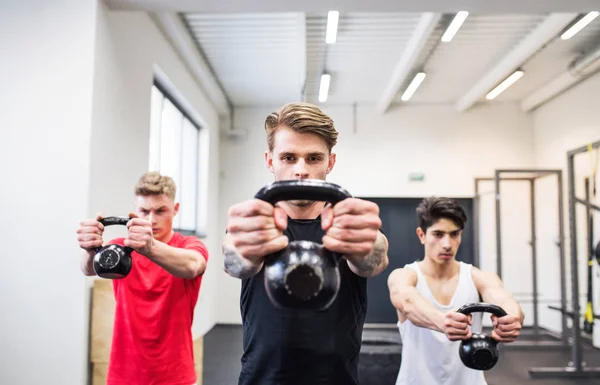 Tre unga män i gymmet gör kettlebell gungor. — Stockfoto