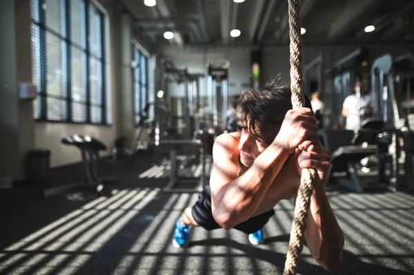 Fit young man in gym working out with climbing rope. — Stock Photo, Image