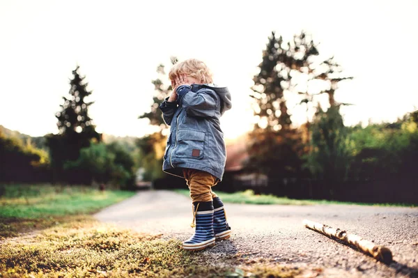 Un niño pequeño parado al aire libre en un camino al atardecer, cubriéndose los ojos . — Foto de Stock