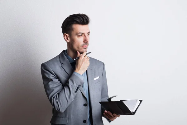 Ritratto di un giovane premuroso con una penna e un diario in studio, pianificazione . — Foto Stock