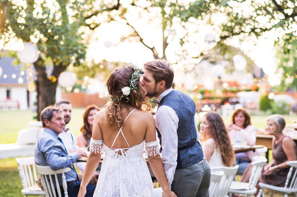 Bride and groom kissing at wedding reception outside in the backyard.