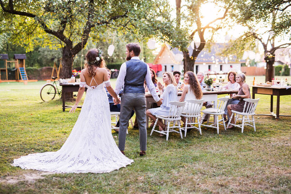 Bride and groom holding hands at wedding reception outside in the backyard.