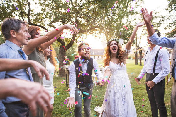 Bride, groom and guests throwing confetti at wedding reception outside.