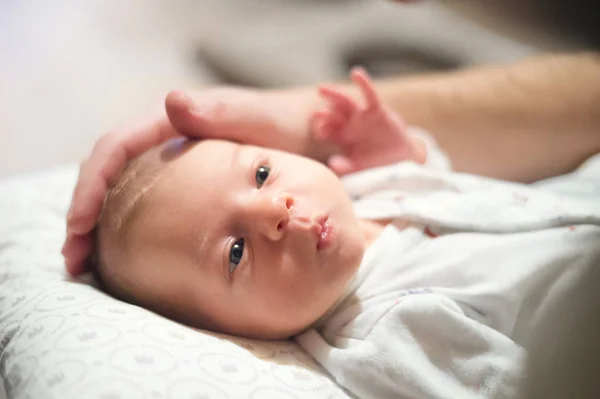 生まれたばかりの赤ちゃんを仰向けにベッド、彼女の頭をなでる認識できない父. — ストック写真