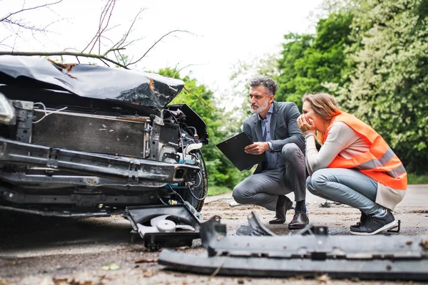 An insurance agent and a woman driver looking at the car on the road after an accident. — Stock Photo, Image